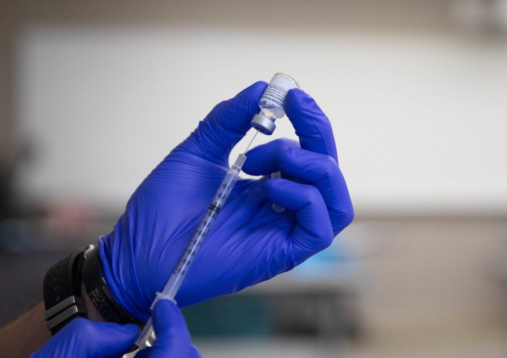 vaccine syringe being held by a hand in a rubber glove