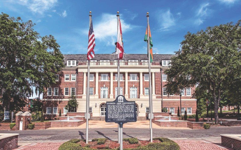Historic sign and flags stand in front of a stately brick building with columns.