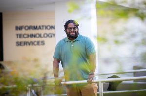 Dominic Perry, A.S. Information Technology graduate from Santa Fe College stands for a portrait wearing a green shirt outside of the IT building..