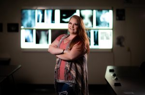 Santa Fe College Radiology student Brittany Lovvorn stands arms crossed in front of a light box filled with x-ray slides, illuminated from behind.
