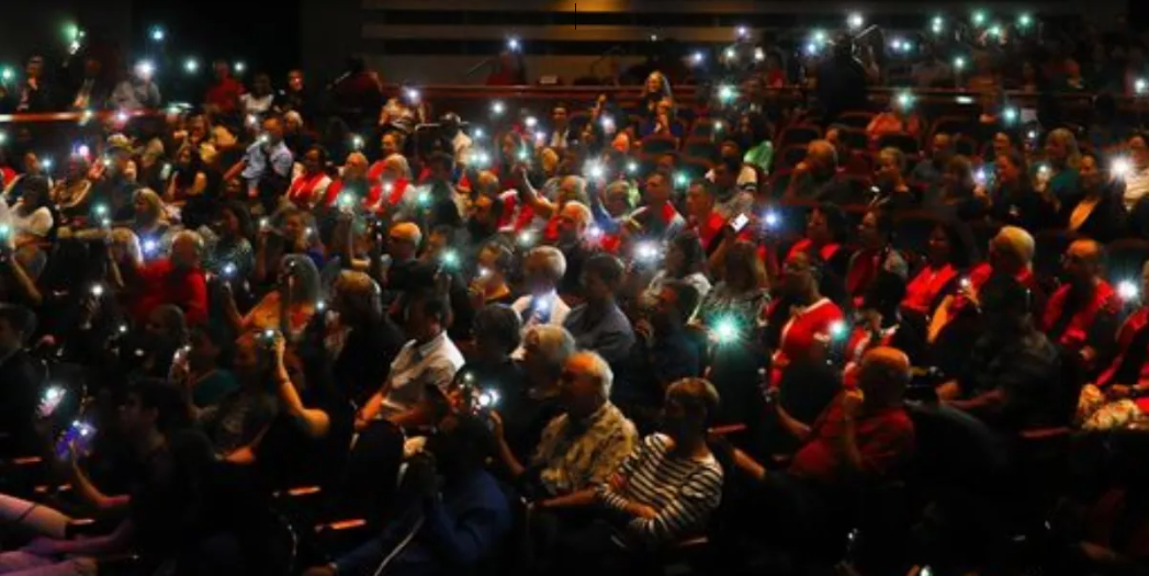 Photo of an audience during convocation at Santa Fe College, lights illuminated from cell phones in a darkened auditorium.
