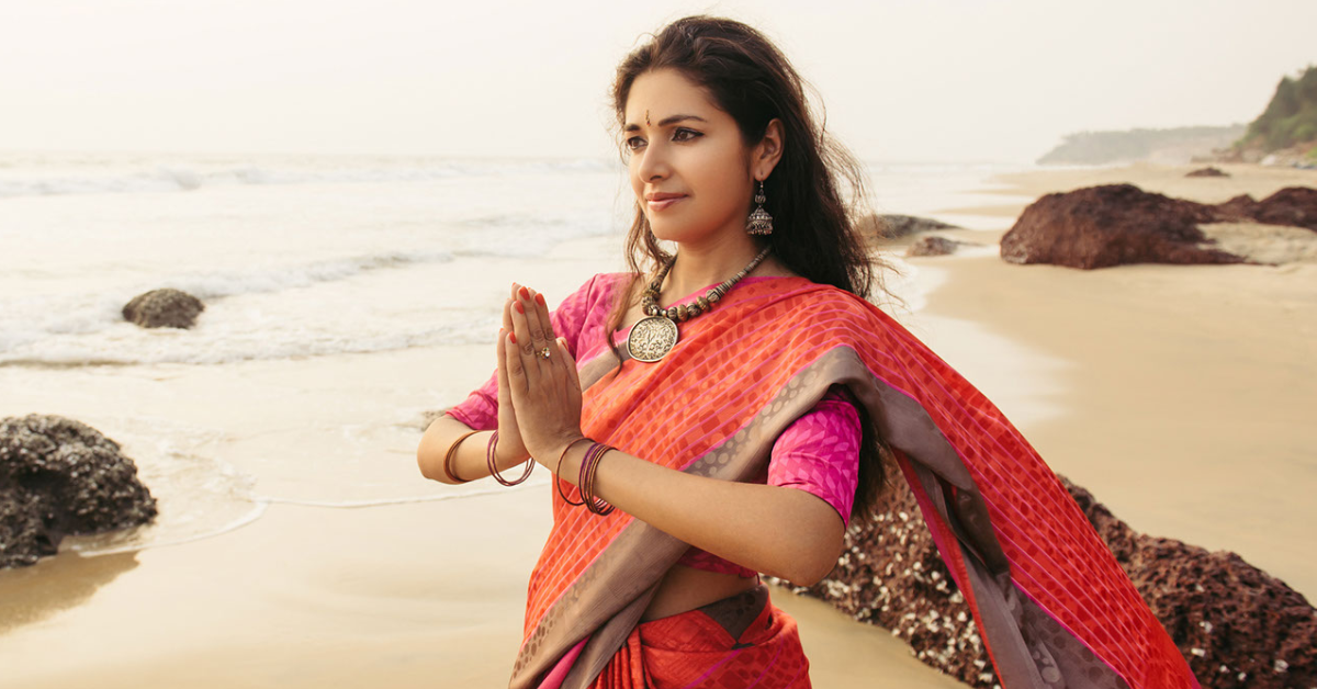 Indian woman on the beach with hands in prayer pose, wrapped in orange.