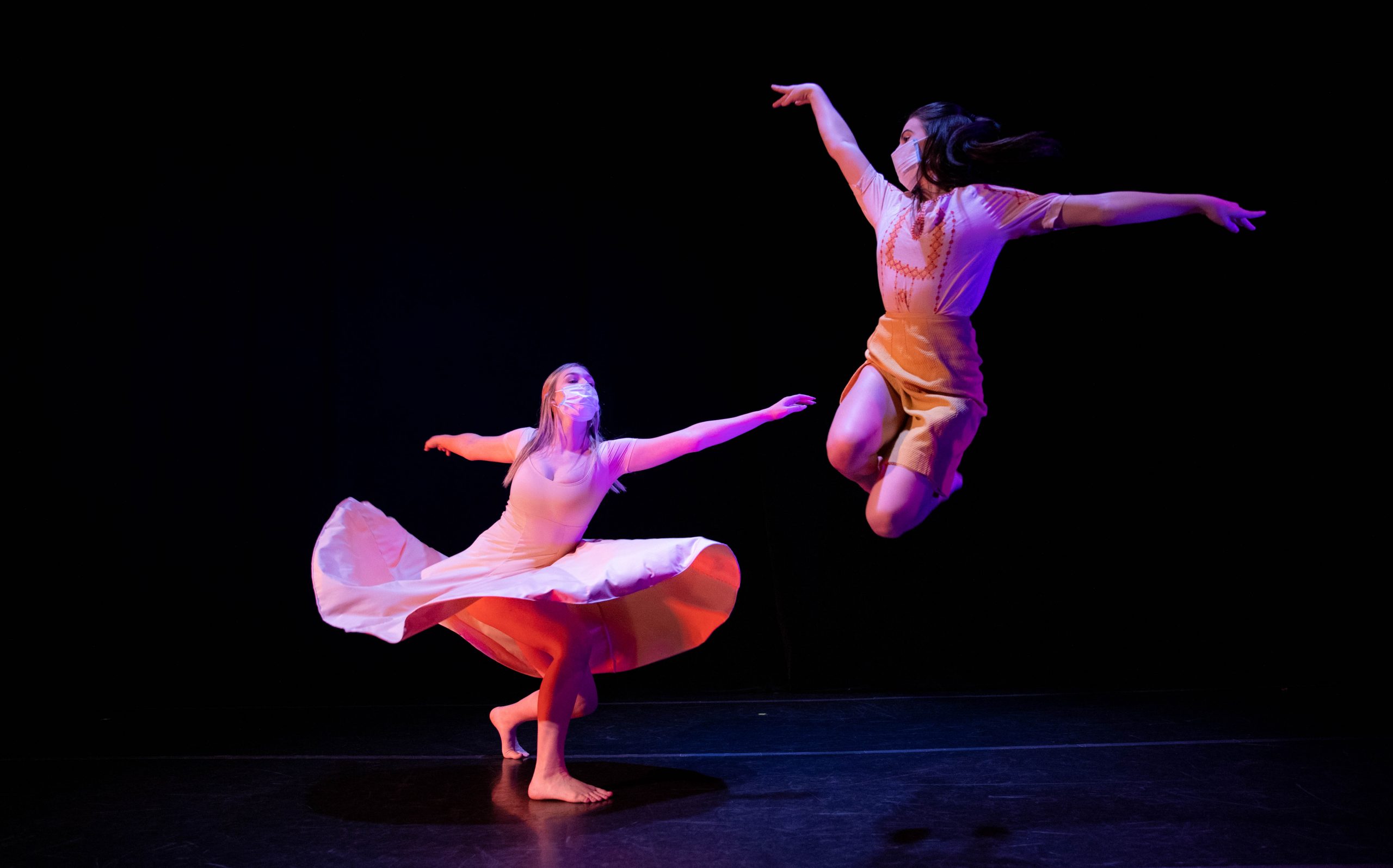 black background, two people dancing, one is leaping in the air, one is twirling, her skirt is flowing