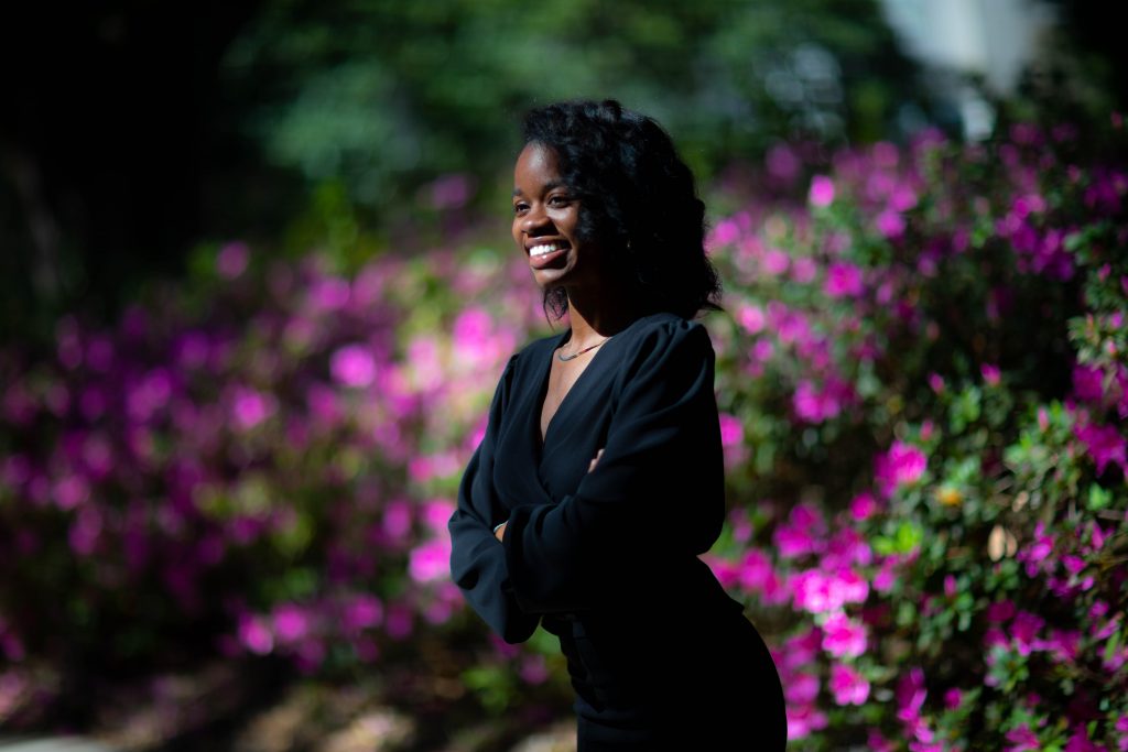 a woman wearing black smiling in front of a bush of pink azaleas