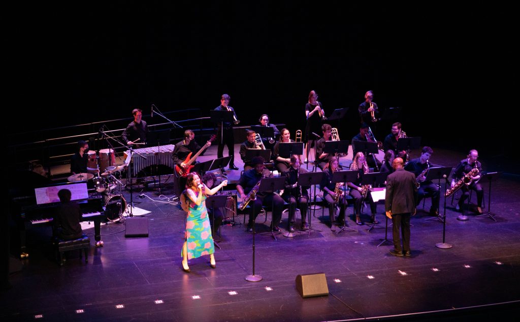 girl in blue dress singing in stage in front of an orchestra