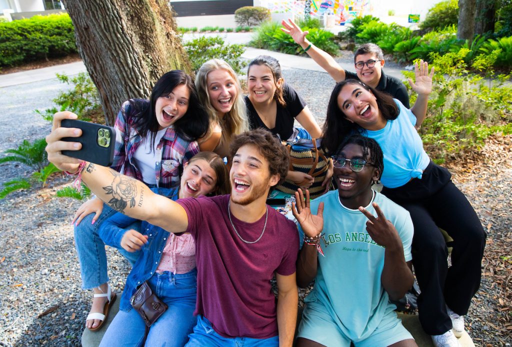 A group of people smile for a selfie as they sit outside together.