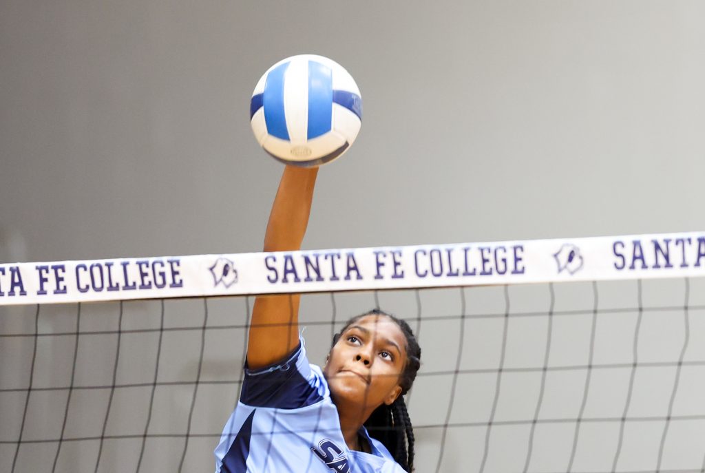 a volleyball player reaching for a ball that is coming over the net