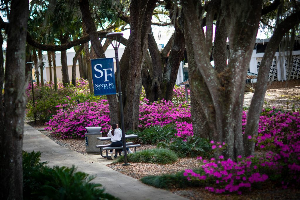 Two Santa Fe College students sit at a bench on the Oak Grove surrounded by blooming azaleas.