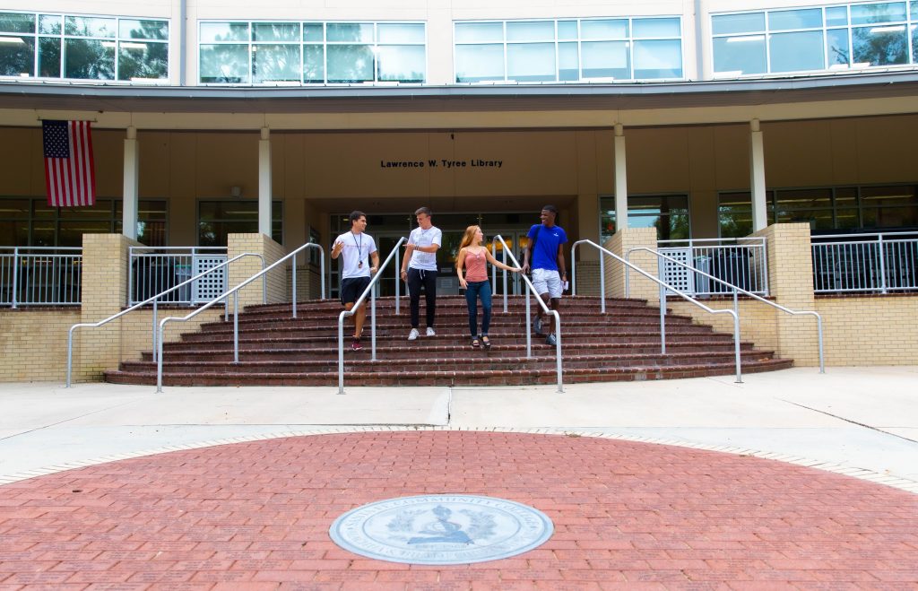 Four students walk down the front steps of the Lawrence W. Tyree Library