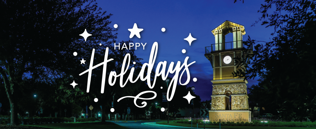 The Santa Fe College clock tower lit up at night text reading "Happy Holidays" to the left of it.