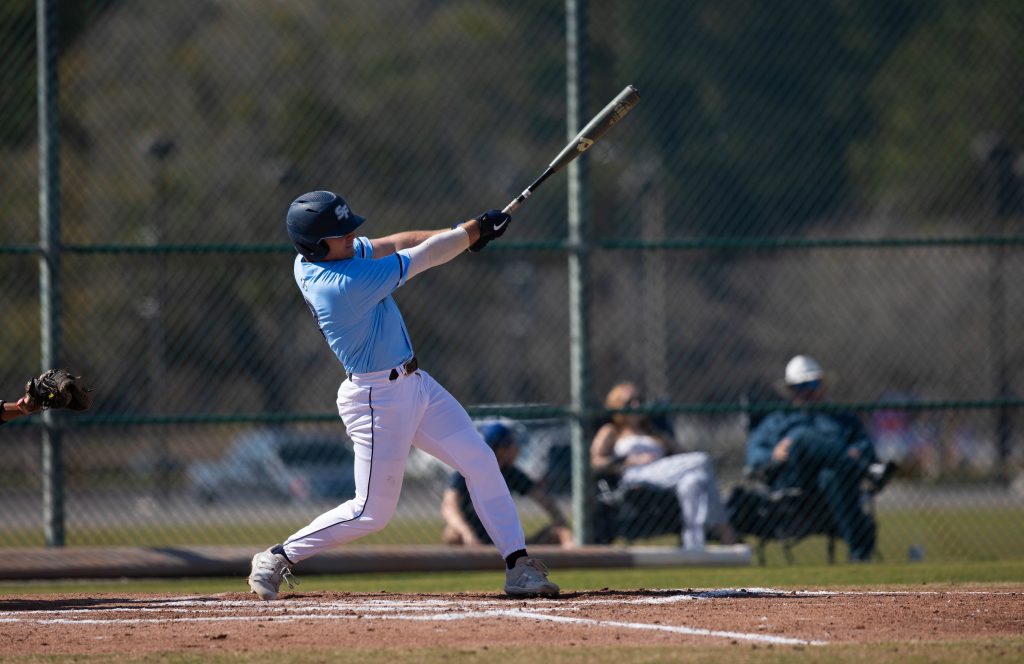 A Santa Fe College baseball player swings at a baseball with a bat during a game.