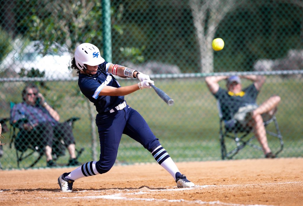 A Santa Fe College softball player swings at a softball with a bat during a game.