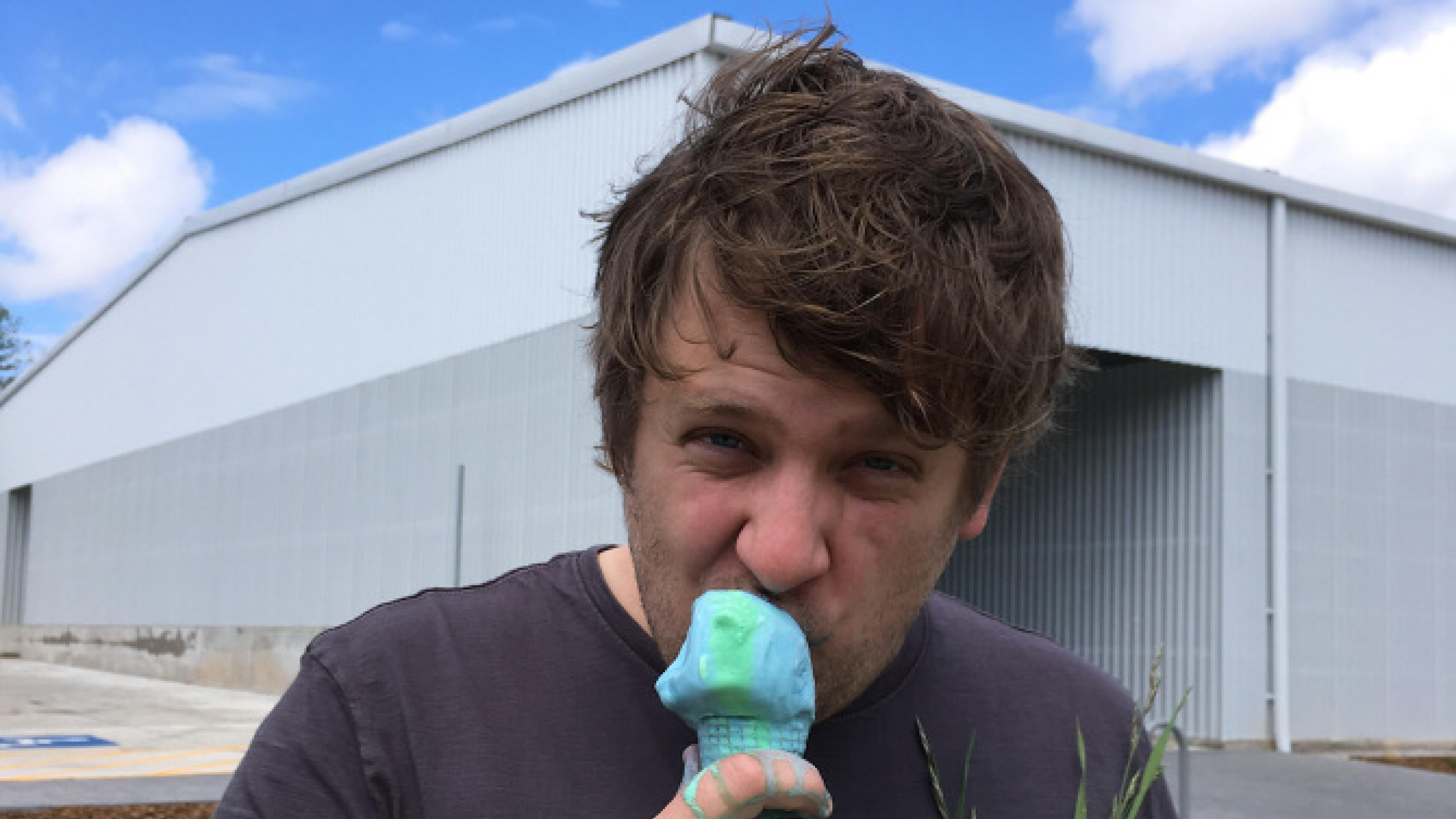 Alexander Hanson eats an ice cream cone in front of a large building outside.