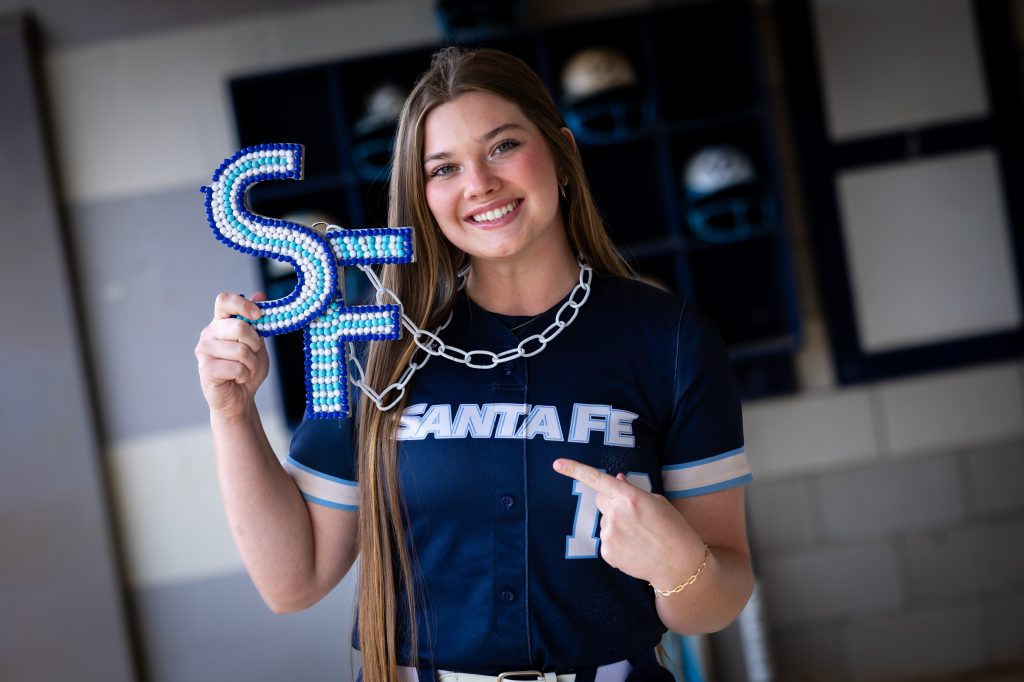 Santa Fe College Saints Softball player Cloey O'Doniel points to the letters "SF" that she is holding up with her other hand.