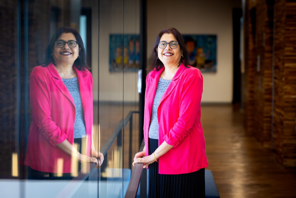 Santa Fe College Associate Professor Dr. Rimjhim Banerjee-Batist smiles while standing next to a window that reflects her image.