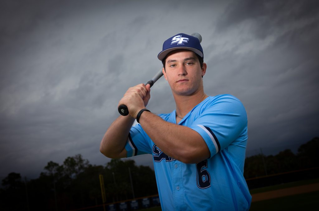 Santa Fe College Saints Baseball player Grant Gallagher holds a baseball bat on his shoulder while he looks into the camera.
