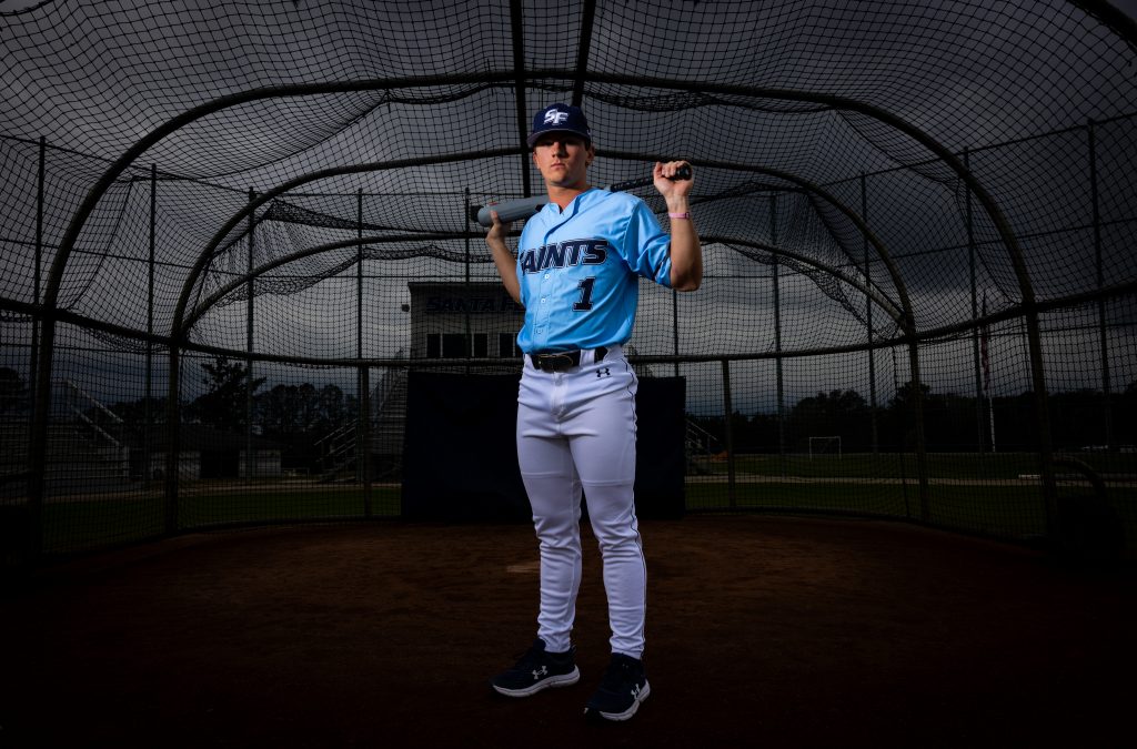 Santa Fe College Saints Baseball player Griffin Sorrow stands holding a baseball bat across his shoulders in front of home plate on a baseball field.