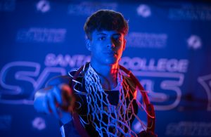 Santa Fe College Saints Men’s Basketball player Kevin Pazmino points at the camera while a basketball hoop is draped across his neck.