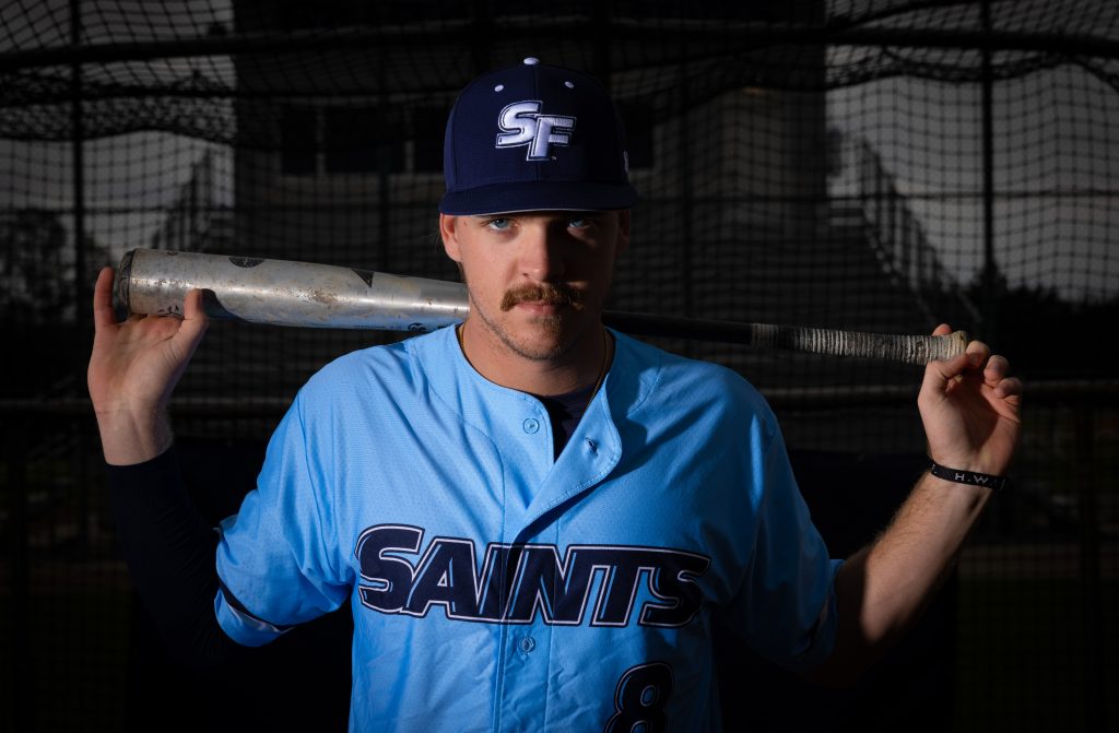 Santa Fe College saints Baseball player Wyatt Campbell holds a baseball bat across his shoulders while staring intently into the camera.