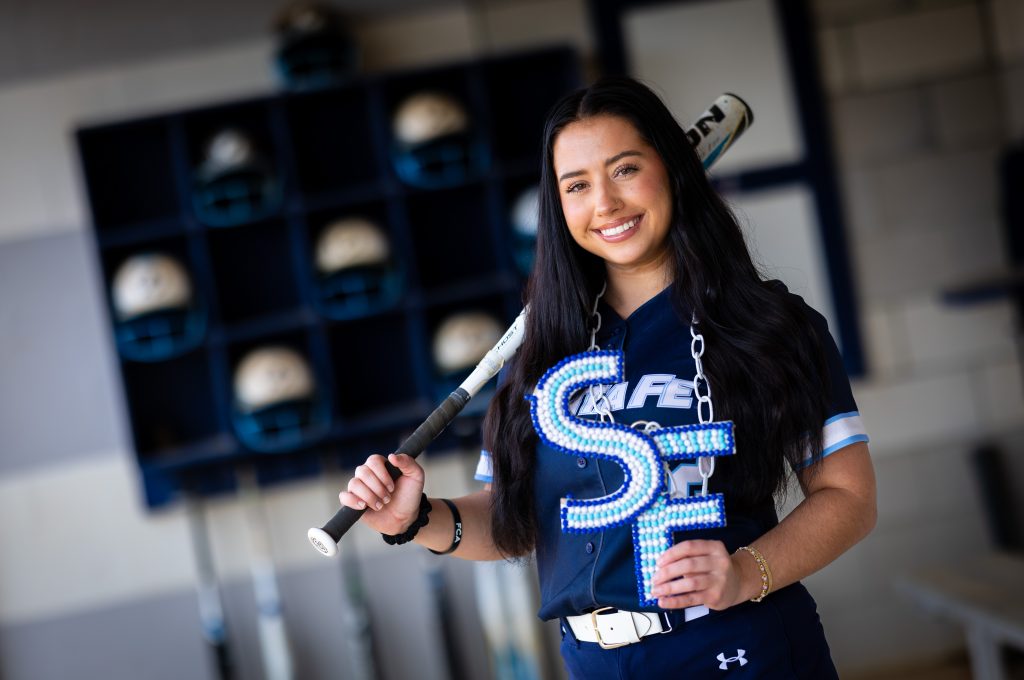 Santa Fe College Saints Softball player Madi Conway holds a bat across one shoulder and the letters "SF" in her other hand.