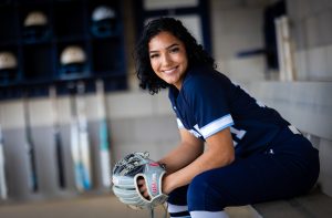 Santa Fe College Saints Softball player Aliana Mercado sits in a dugout while wearing a softball mitt.