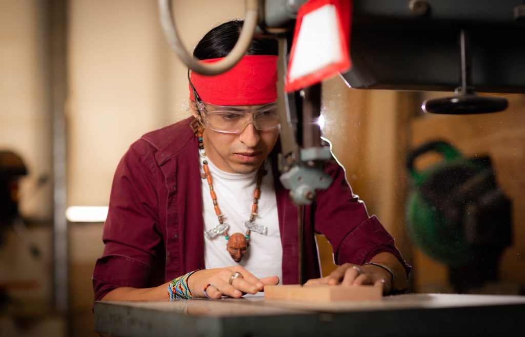 Santa Fe College Professor Mario Mutis sits at a workbench working on a project.