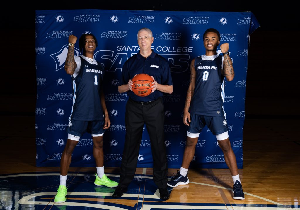 Coach Mowry stands in between two Santa Fe College basketball players while holding a basketball.