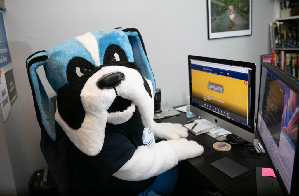 Caesar Saint, Santa Fe College's mascot, sits at a desk with two computer monitors.
