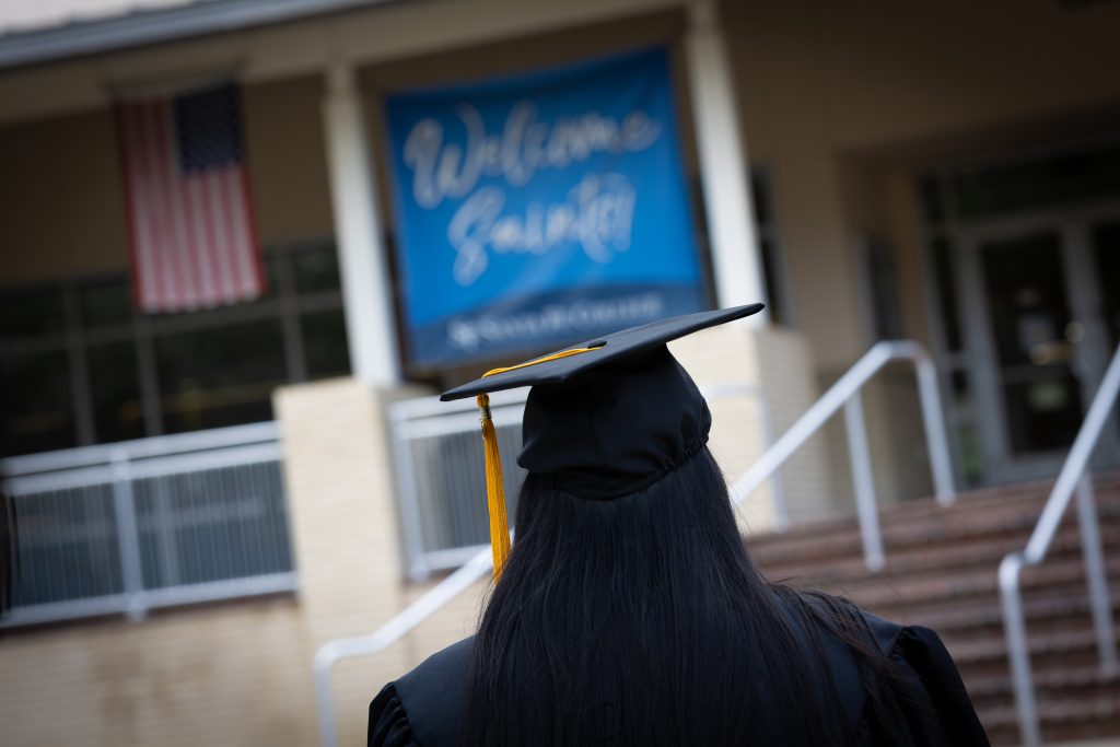 Santa Fe College graduate and University of Florida student Rafa Hossain wears a graduation cap and gown while facing a building.