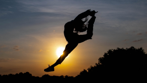 A dancer jumping into the air with the sun behind them.