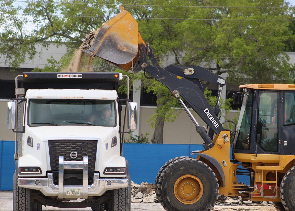 A bulldozer unloads debris into a dump truck.