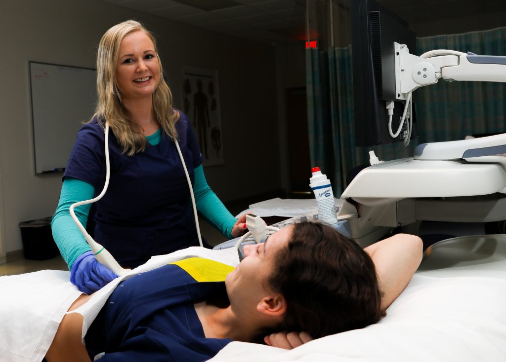 A person in a medical uniform standing over a patient in a hospital setting.