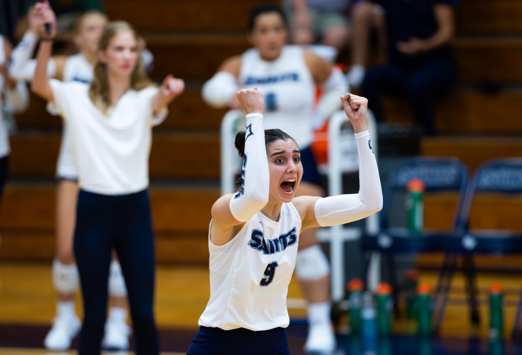 A person in a white jersey cheering at volleyball game.