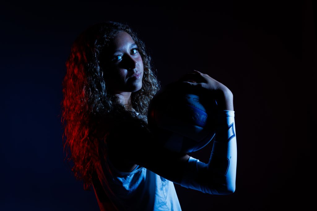 An individual holding a volleyball on their bicep in a dimly-lit environment.