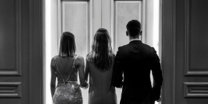 Three individuals with their backs to the camera stand in front of a closed door, suggesting anticipation or waiting.