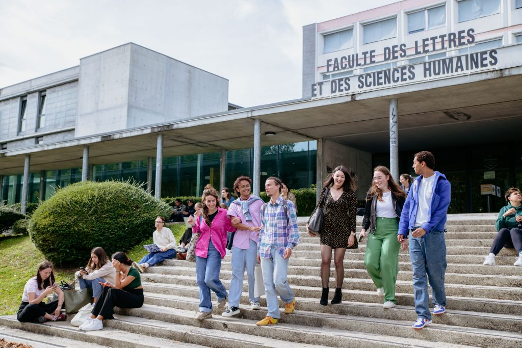 Students sitting and walking down the steps of the 'Faculté des Lettres et des Sciences Humaines' building, a historic academic structure with tall columns and French signage.